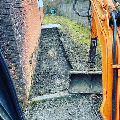 An orange excavator in a yard next to a brick wall.