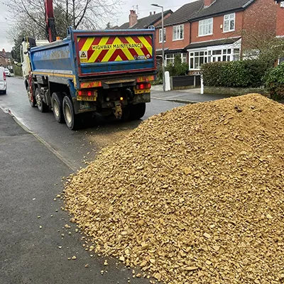 A dump truck driving down a street next to a pile of wood chips.